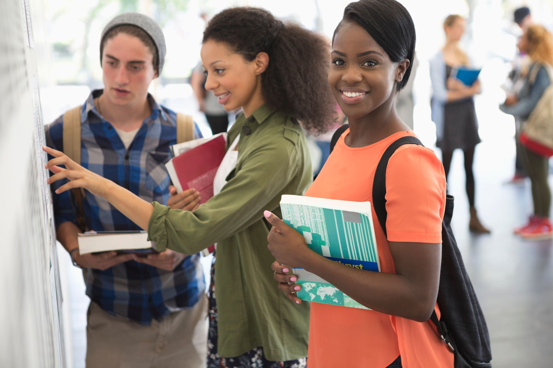 Female student smiling at camera with two other students looking at notice board