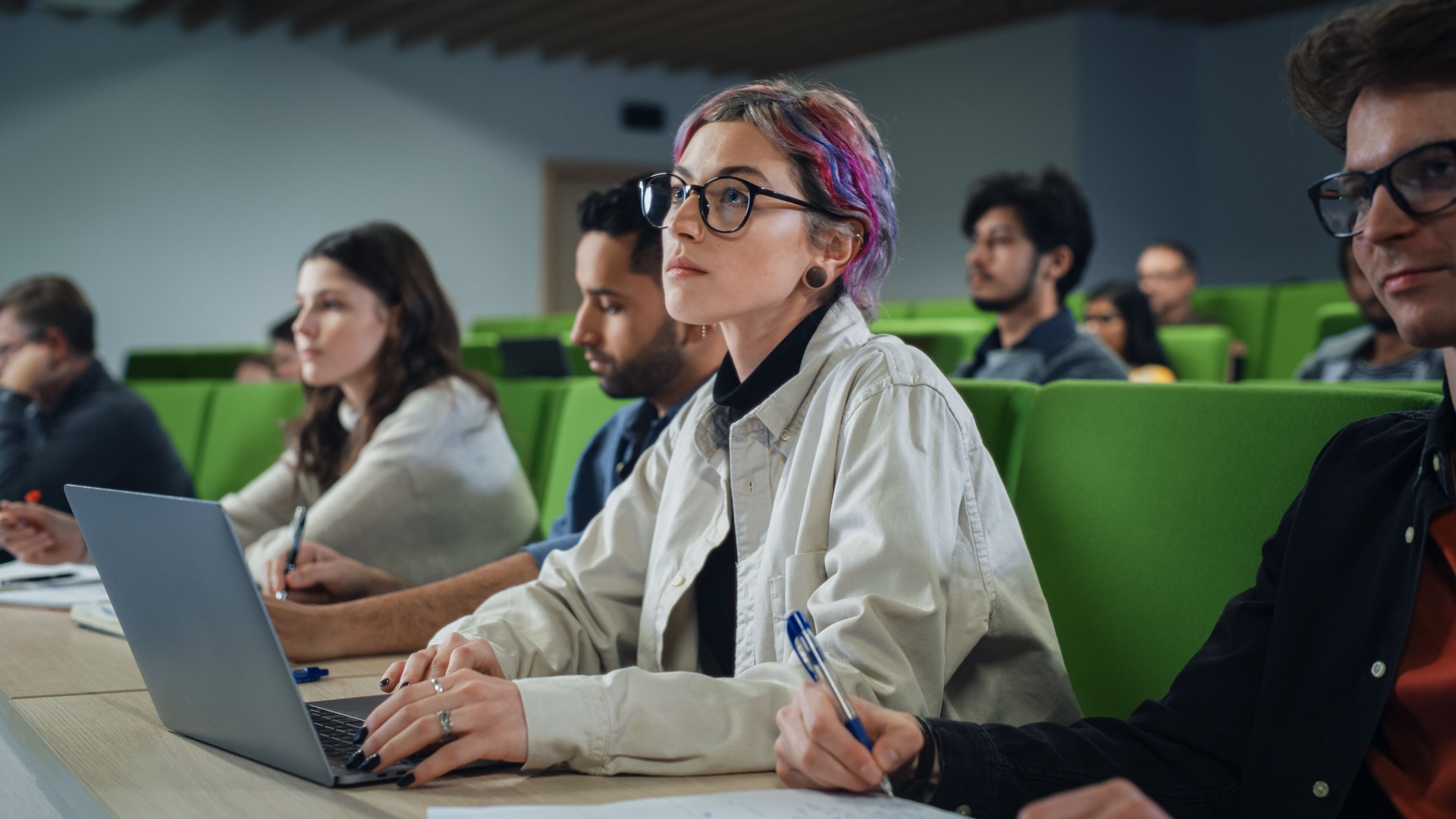 Smart Creative Female Student Studying in University with Diverse Multiethnic Classmates. Young Woman with Colored Short Hair is Using a Laptop Computer. Taking Notes from a Lecture in College